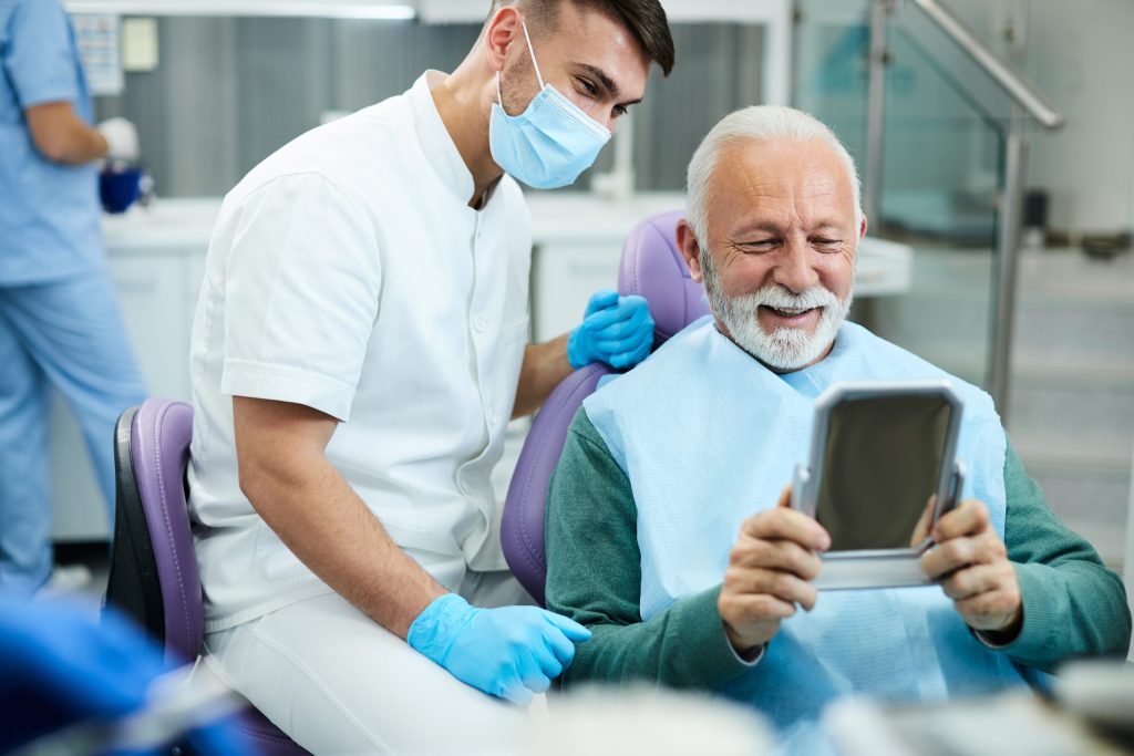 Senior patient smiling at his new dentures in a hand mirror