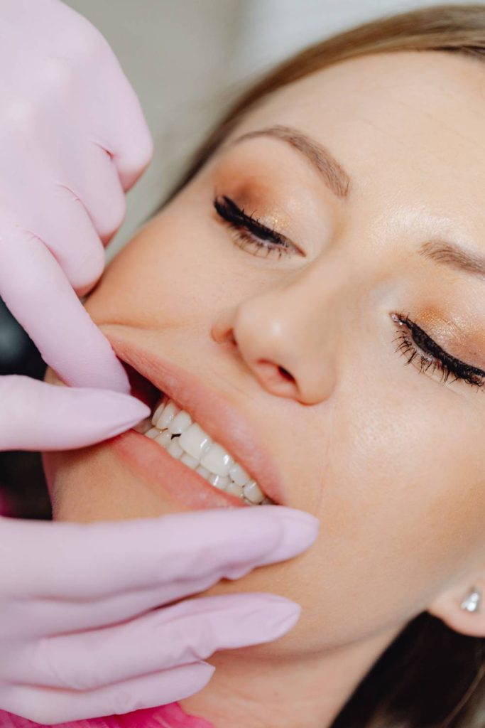 Dental professional wearing pink gloves performs intraoral examination on relaxed female patient showing front teeth