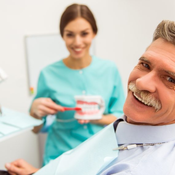 Dental assistant showing a denture model to a smiling senior patient